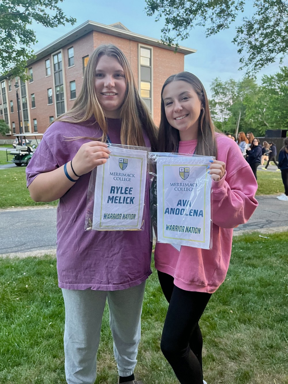 Rylee and Ava posing with their banners at Merrimack's new student orientation on 6/20/22.