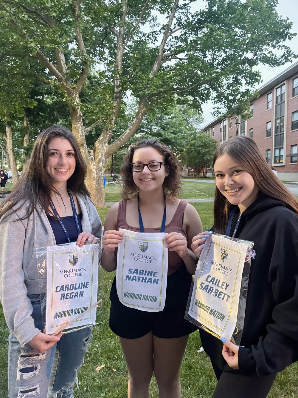 Cailey, Sabine, and Caroline holding their personalized banners at Merrimack College new student orientation on 6/20/22.